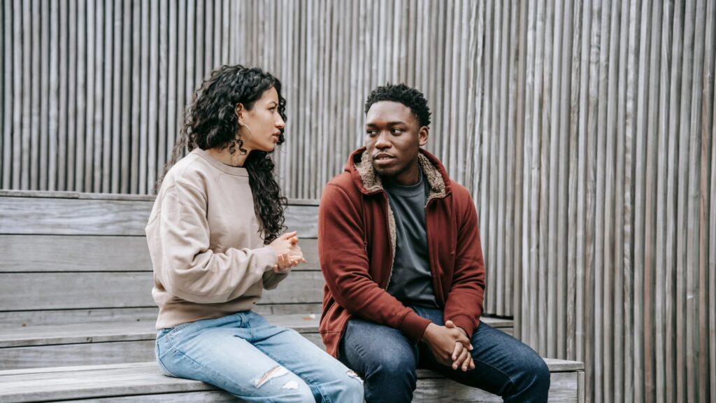 A young woman talking to a you man sitting on wooden stairs